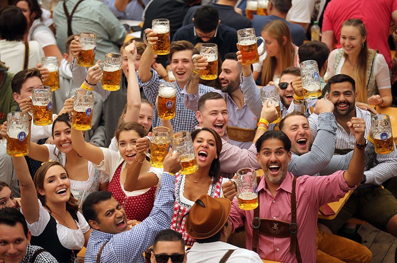 A joyful Oktoberfest crowd in dirndls and lederhosen raising full beer steins in a toast