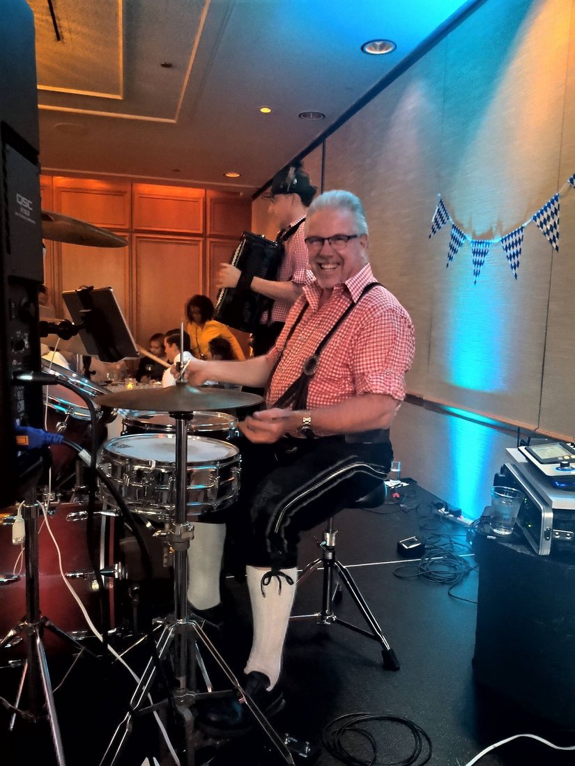 John Gunther at the drums during a banquet performance, the accordion behind him and Bavarian bunting on the wall
